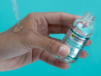 Hand with Garnier face serum Hyaluronic Acid on palm and holding bottle. On a turquoise background.