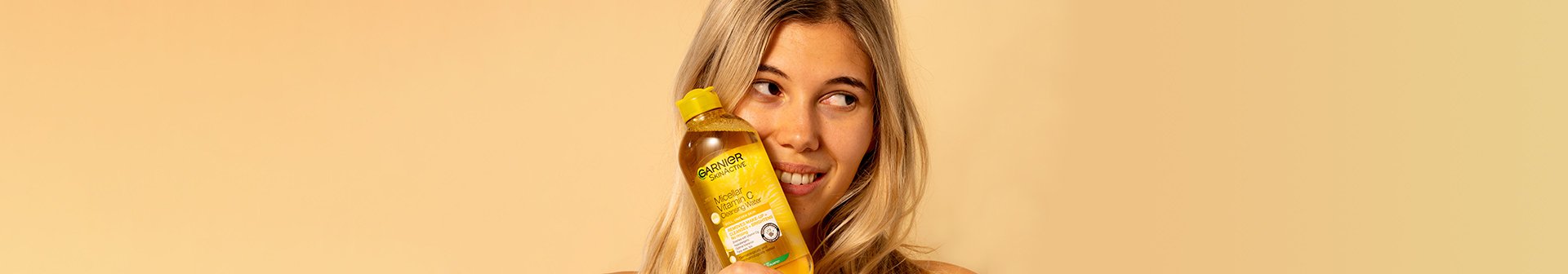 Blonde female holding vitamin c micellar water against face