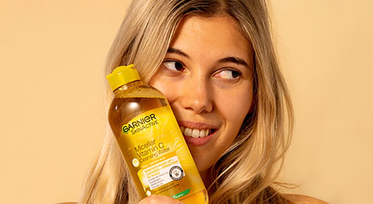 Blonde female holding vitamin c micellar water against face