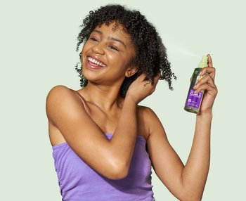 a curly-haired woman using a spray to style and refresh her curls in the morning