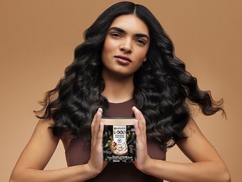 Image of model on brown background. Model is holding Garnier GOOD product in hands in shade 3.0